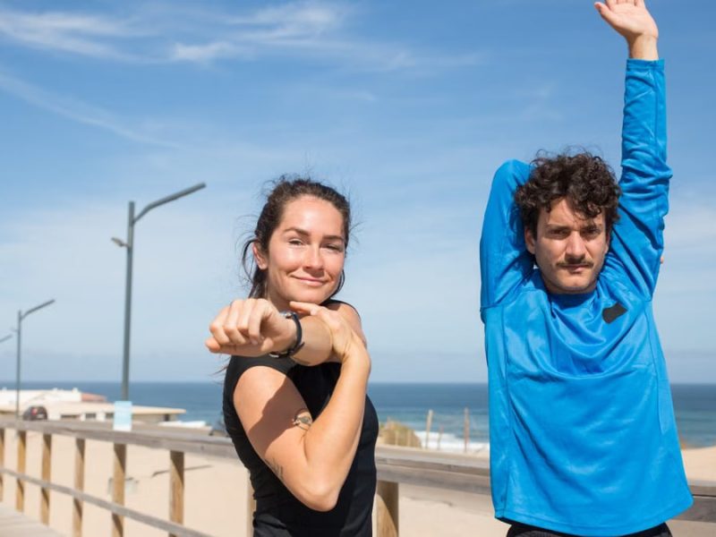 Active young couple stretching outdoors by the ocean on a sunny day in Portugal.
