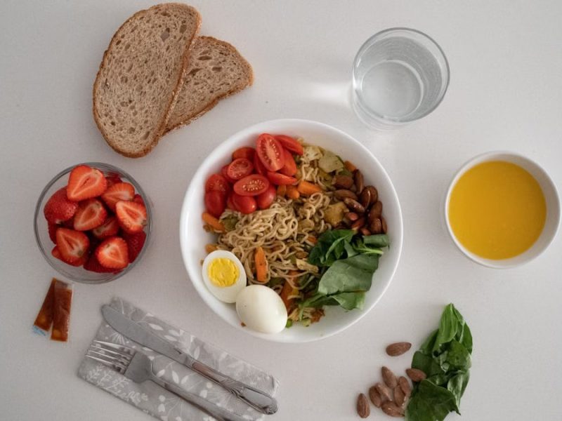 A balanced meal featuring a variety of healthy ingredients including noodles, eggs, almonds, strawberries, and fresh vegetables.