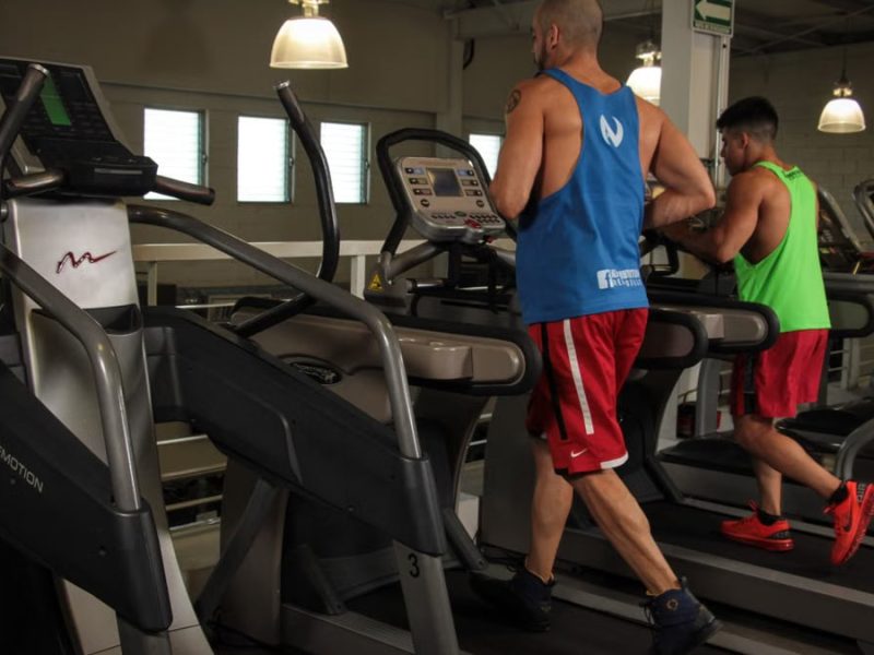 Two men running on treadmills in a modern gym, promoting fitness and health.